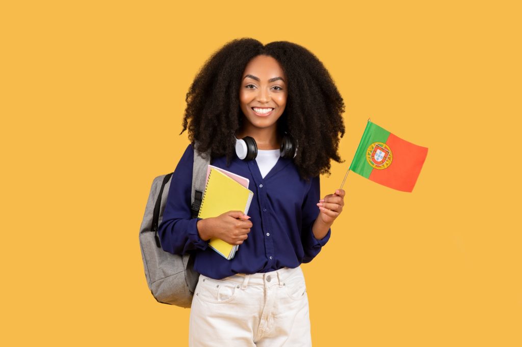 Joyful black student with Portuguese flag and notebooks on yellow background